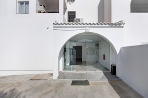 Entrada d'un edifici amb una porta de vidre, un sòl de rajola i un petit escaló que hi mena.
