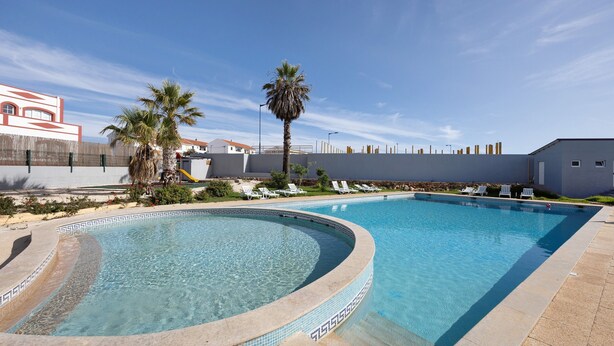 Una piscina de borde curvo, palmeras y sillas de descanso.