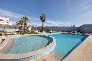 Una piscina de vora corbada, palmeres i gandules.