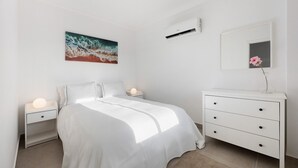 A bedroom with a bed, bedside tables, a dresser, a painting, and an air conditioning unit. - Apartment "Victoria's House" with Shared Pool & Wi-Fi (Sagres)