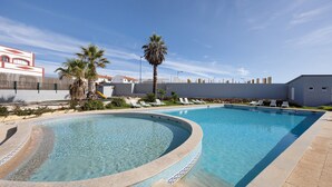 A swimming pool with a curved edge, palm trees, and lounge chairs. - Apartment "Victoria's House" with Shared Pool & Wi-Fi (Sagres)