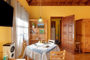 Un coin repas avec une table dressée pour deux personnes, une chaise en bois, une bibliothèque remplie de livres et une plante, ainsi qu’une porte en bois.