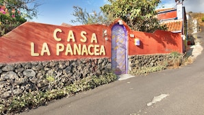 Un mur de pierre sur lequel est apposée une enseigne indiquant « CASA LA PANACEA », et une porte violette.