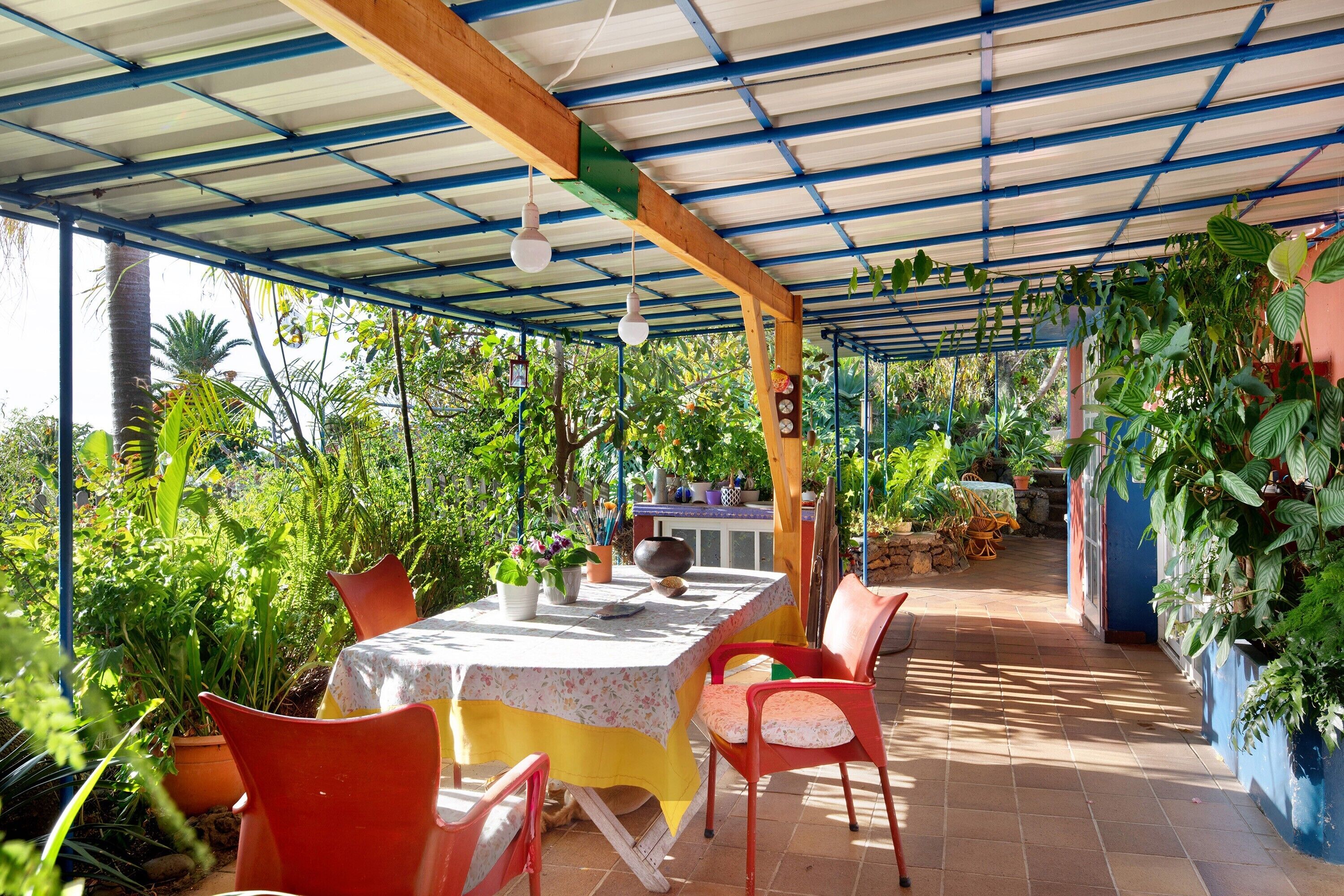 A covered patio area with a table and chairs, surrounded by potted plants and a view of the garden.