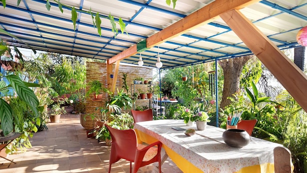 Un patio couvert avec une table et des chaises, entouré de plantes en pot et doté d’un sol en briques.
