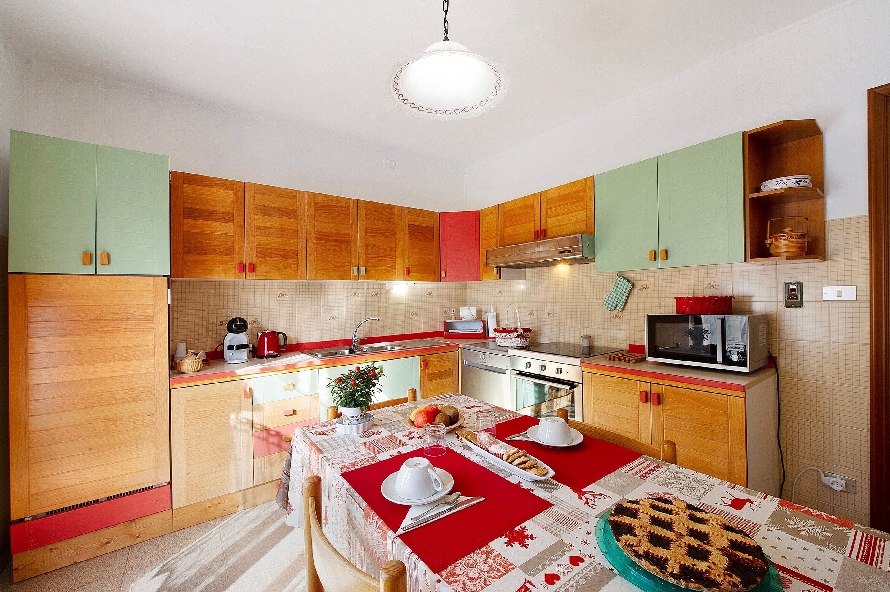 Una cocina con armarios de madera, microondas, estufa y una mesa de comedor con platos y una tarta.