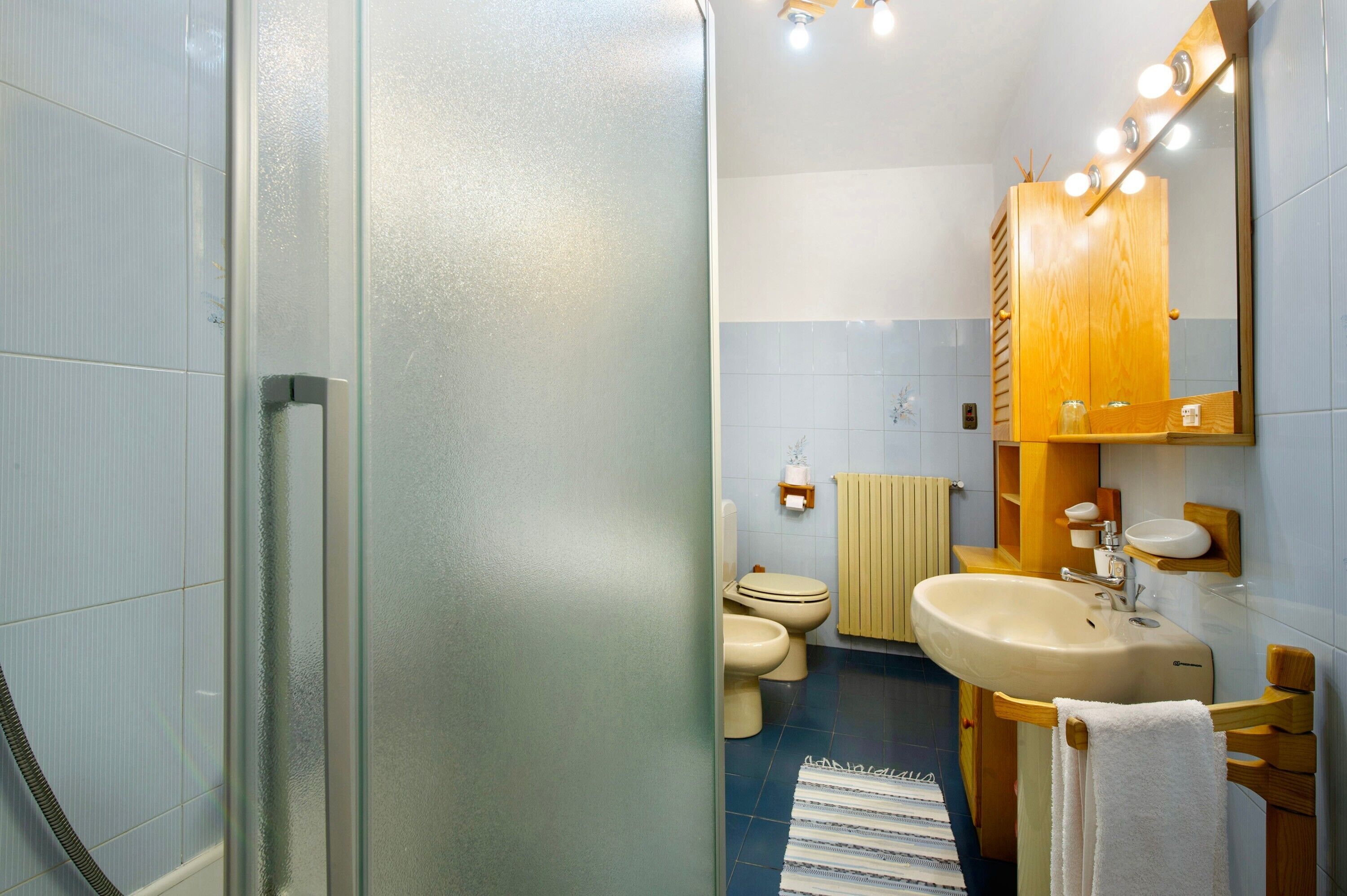 A bathroom with a glass shower door, a sink, a toilet, and a mirror with lights.