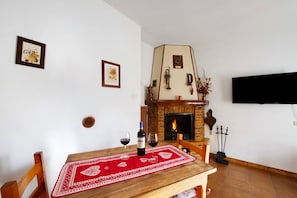Un comedor con chimenea, una mesa con mantel rojo y dos copas de vino tinto.