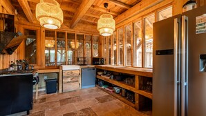 A modern kitchen with wooden beams, a stainless steel refrigerator, and a stone-tiled floor.