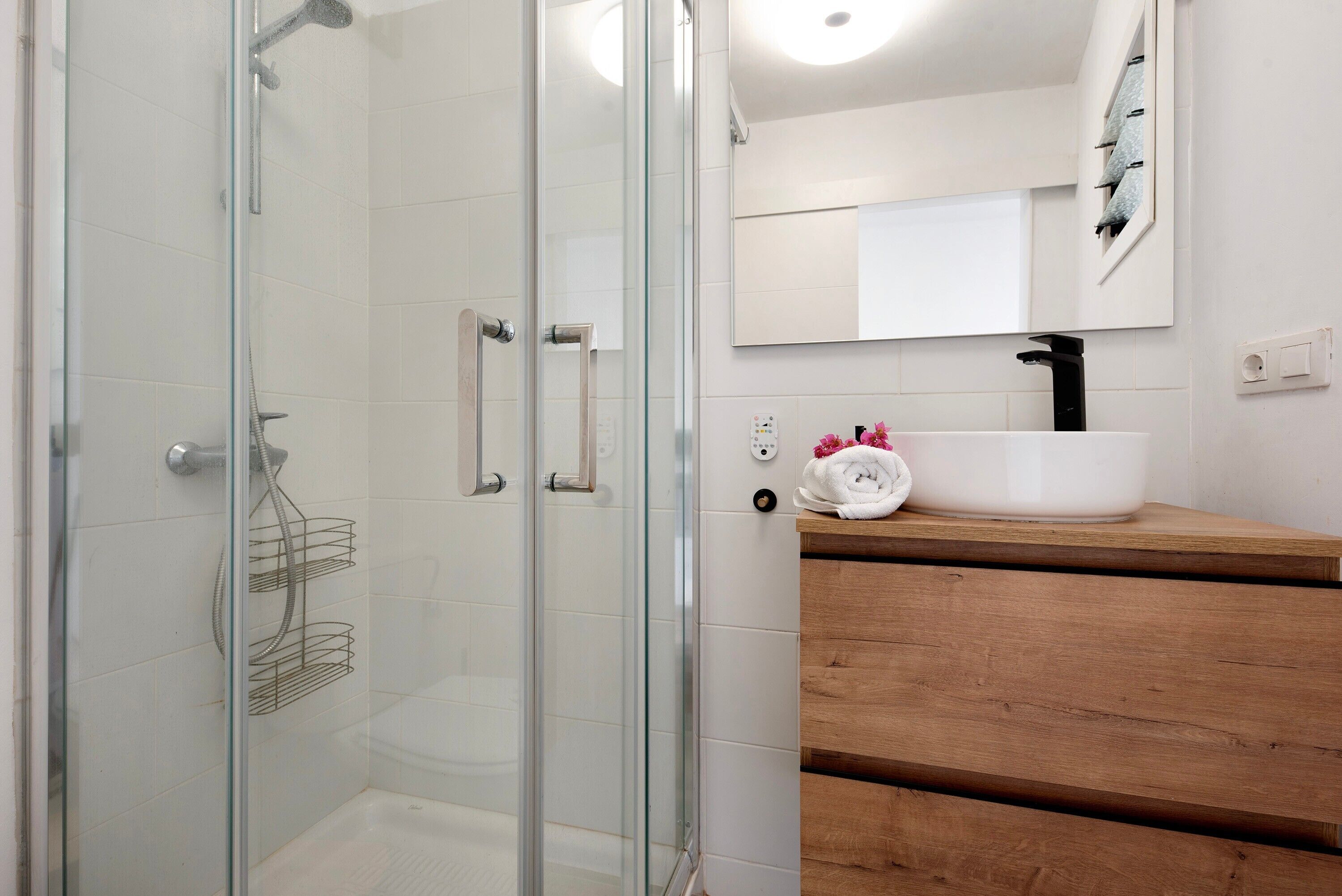 A modern bathroom with a glass shower enclosure, a white sink with a black faucet, and a wooden vanity.