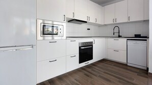 Una cocina moderna con armarios blancos, horno empotrado, lavavajillas y microondas.