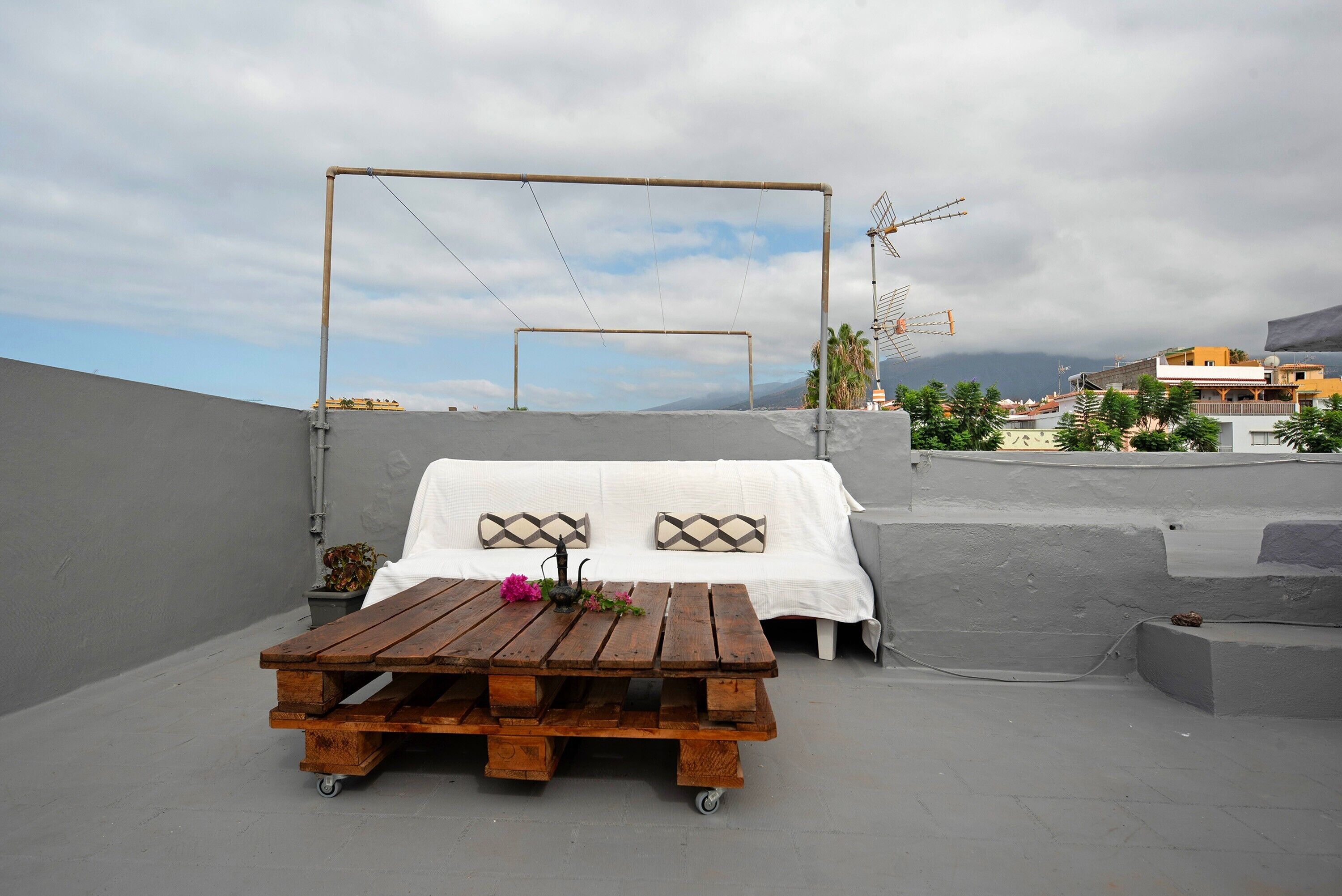A rooftop terrace with a wooden table, white sofa, and a view of the cityscape.