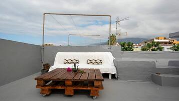 A rooftop terrace with a wooden table, white sofa, and a view of the cityscape.