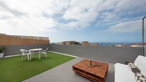 Una terraza en la azotea con una mesa de comedor, sillas, una mesa de centro de madera y un sofá.