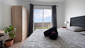 Un dormitorio con cama, planta en maceta, armario, mesita de noche y vistas al exterior.