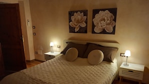 A neatly made bed with a quilted cover, two wall-mounted lamps, and two large floral paintings above the bed. - Casa Clery Tuscan Style Breakfast Included (Montelupo Fiorentino)
