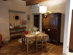 Un coin repas comprenant une table en bois, des chaises, un lustre, un buffet et une étagère murale agrémentée d’objets décoratifs.