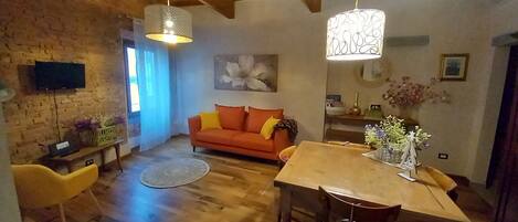 A cozy living room with a wooden ceiling, a sofa, a dining table, and a TV mounted on the wall.