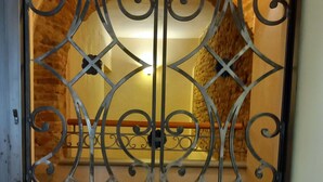 A metal gate with intricate designs, a brick wall, and a light fixture in the background. - Casa Clery Tuscan Style Breakfast Included (Montelupo Fiorentino)