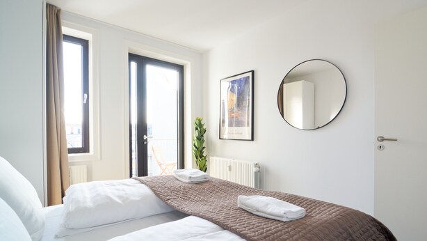 A hotel room with a bed, a round mirror, a framed picture, and a window with curtains. - Nørre Voldgade 80 (Copenhagen)