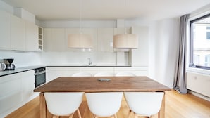 A modern kitchen with white cabinets, a wooden dining table, and pendant lights. - Nørre Voldgade 80 (Copenhagen)