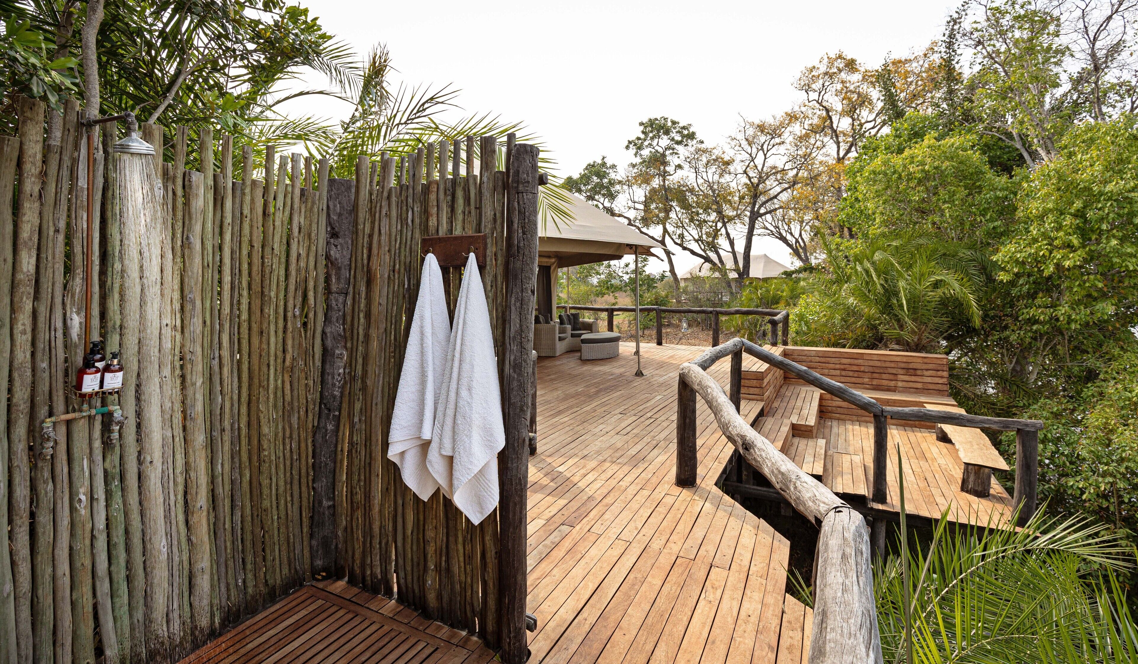 A wooden deck with a wooden fence, a towel hanging on the fence, and a bench.