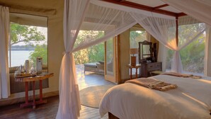 Une chambre avec un grand lit, une table en bois sur laquelle est disposé un service à thé, et une vue sur une terrasse et l’eau.