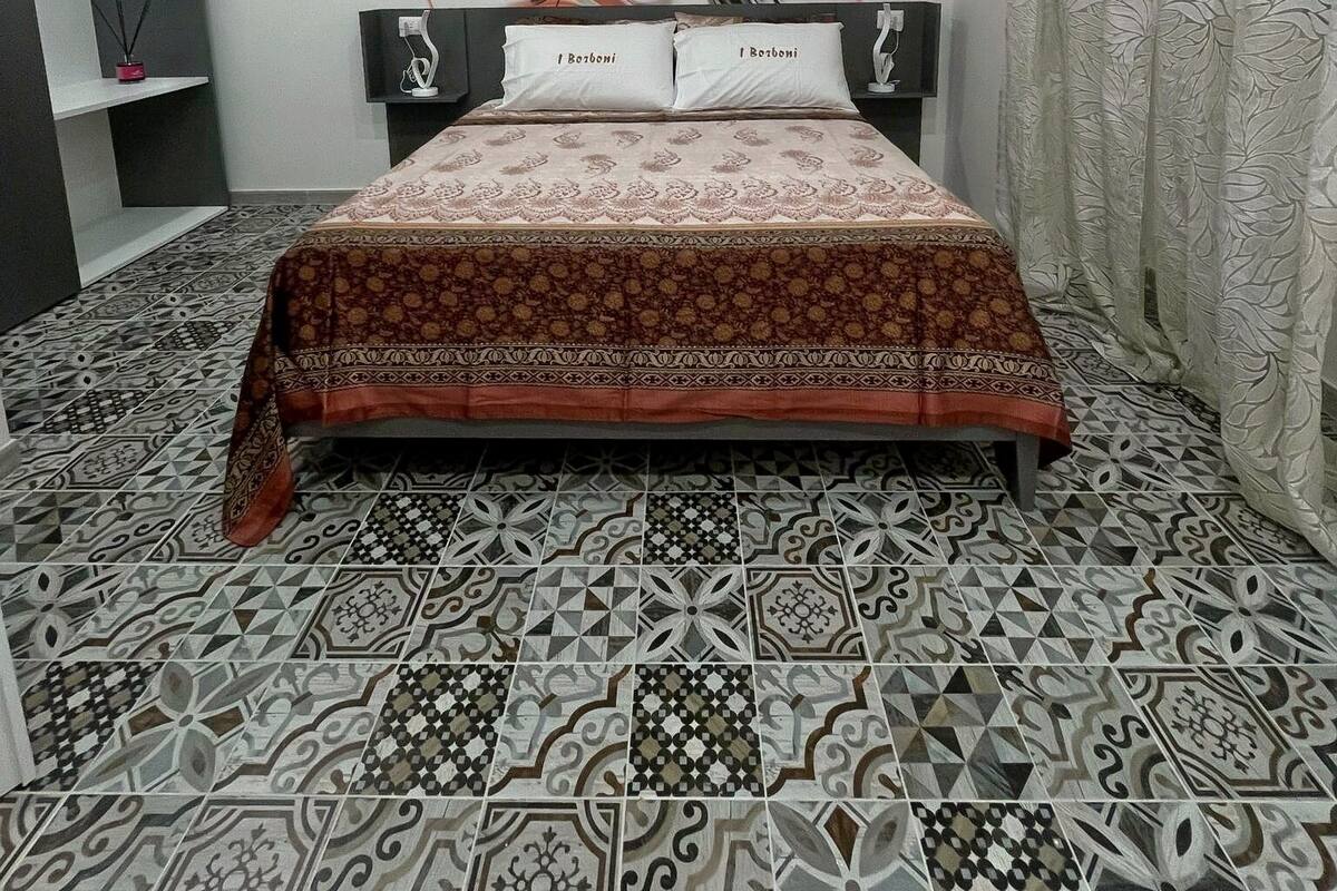 A bedroom with a patterned bedspread, a large wall mural, and a geometric patterned floor.