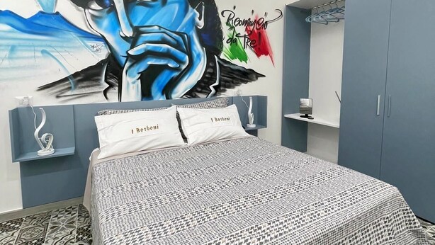 A bedroom with a large mural, a bed with patterned bedding, a wardrobe, and a mirror. - B&B i borboni (Naples)