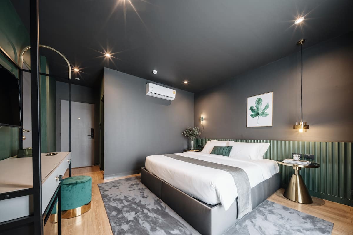 A modern bedroom with a large bed, a bedside table, a mirror, and a wall-mounted air conditioner.