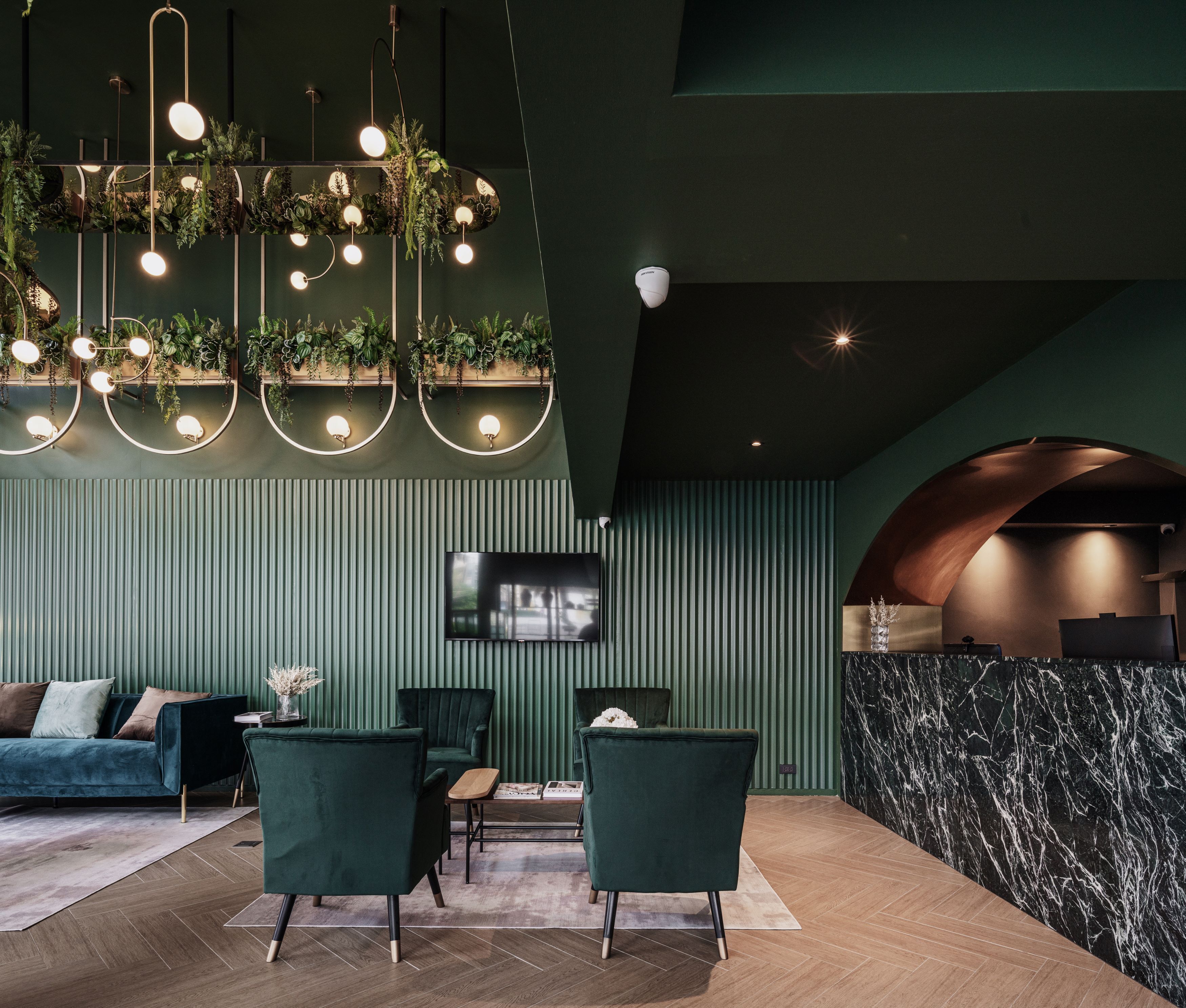 Een moderne lounge met een groen kleurenschema, met een bank, twee fauteuils, een salontafel en een aan de muur bevestigde televisie.