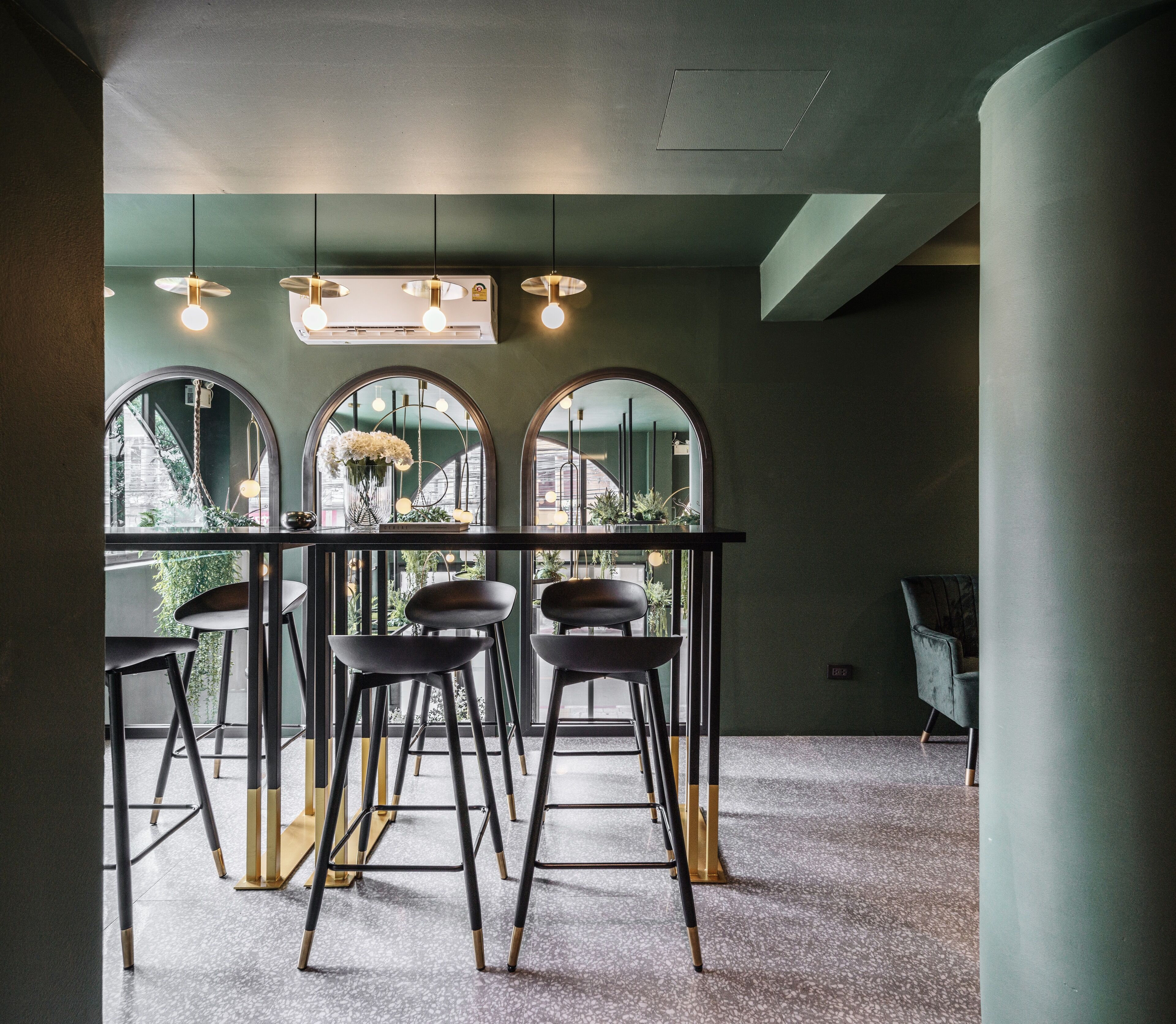 A modern bar area with a long counter, three stools, and a large mirror with arched top.