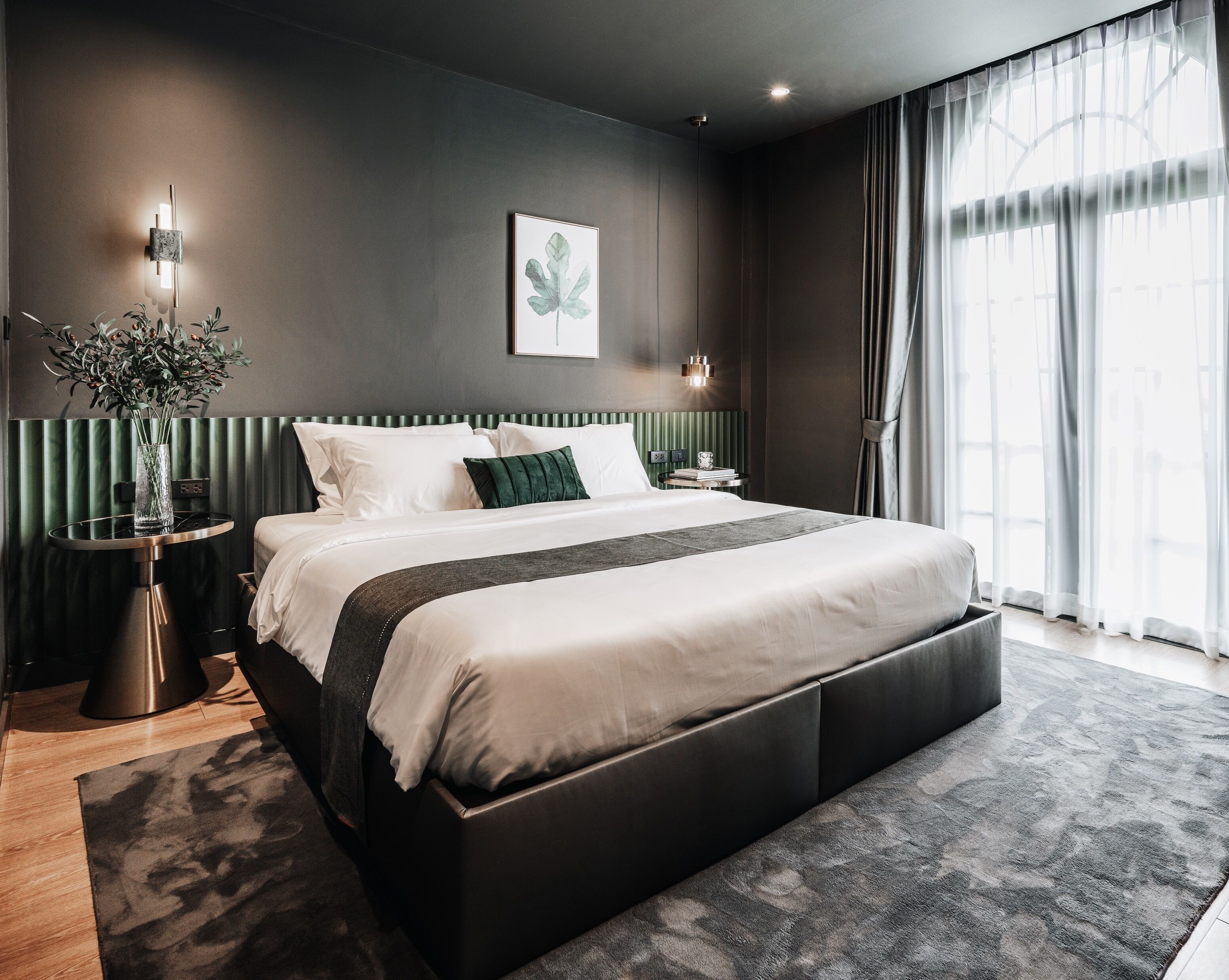 A modern bedroom with a large bed, a bedside table, a wall-mounted light, and a window with curtains.