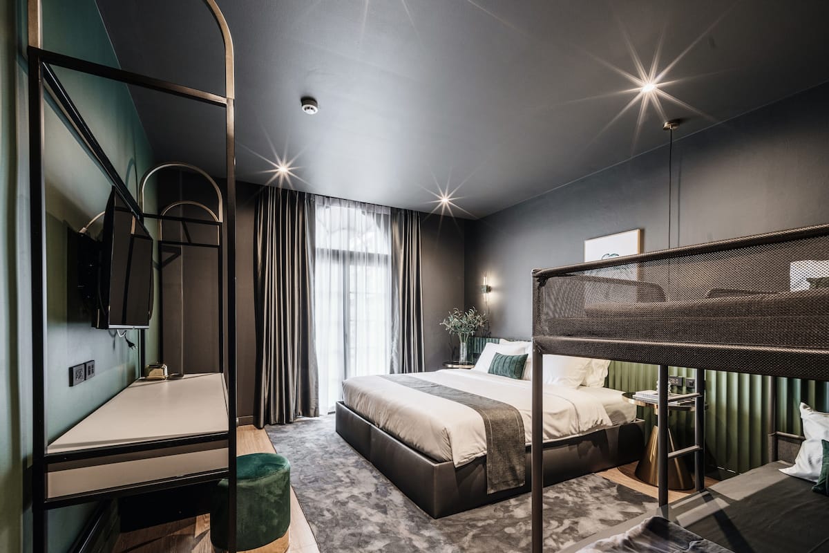A modern hotel room with a large bed, a desk, a chair, and a bunk bed.