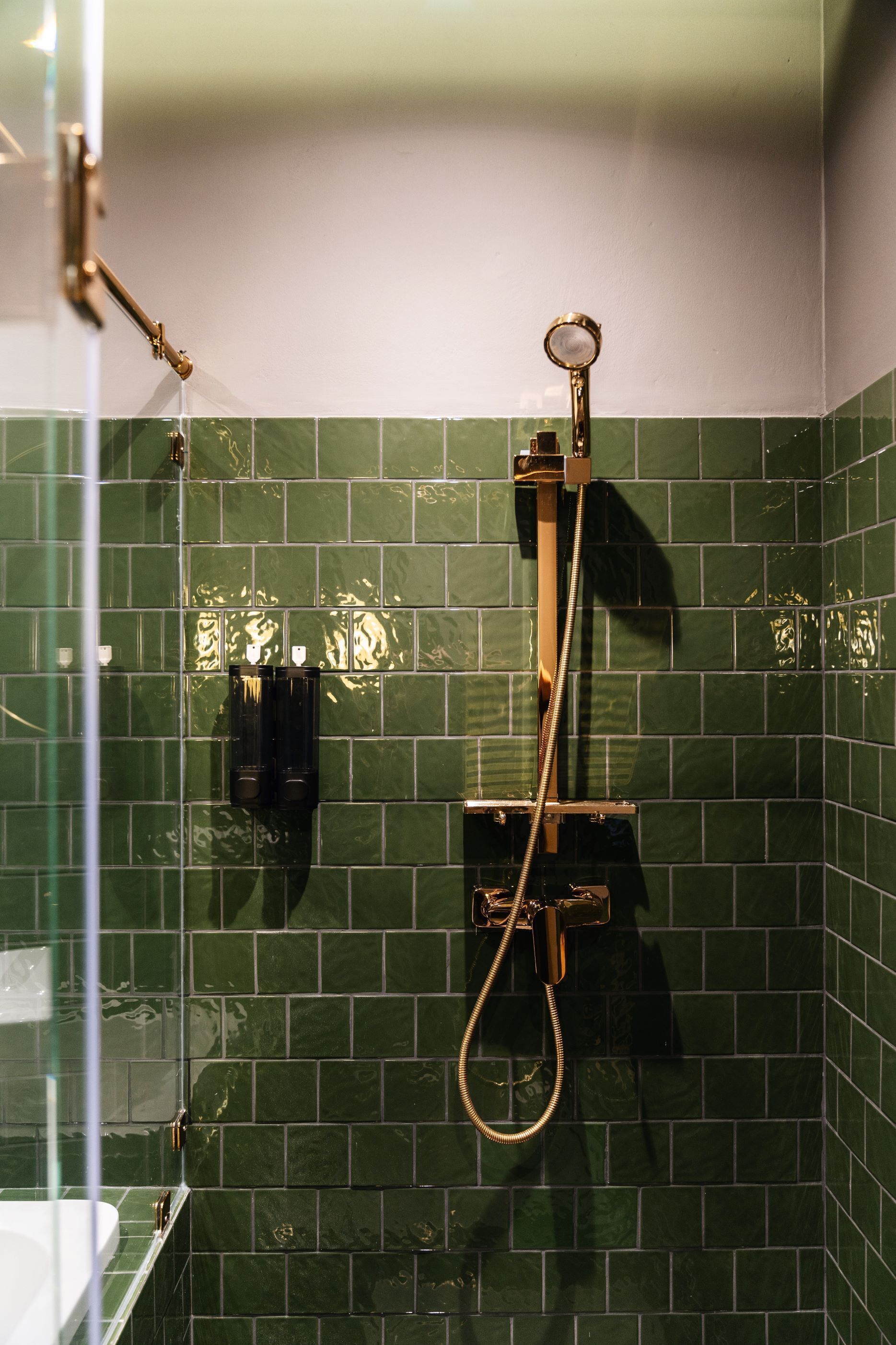 Um banheiro com paredes revestidas de azulejos verdes, box de vidro e chuveiro manual.