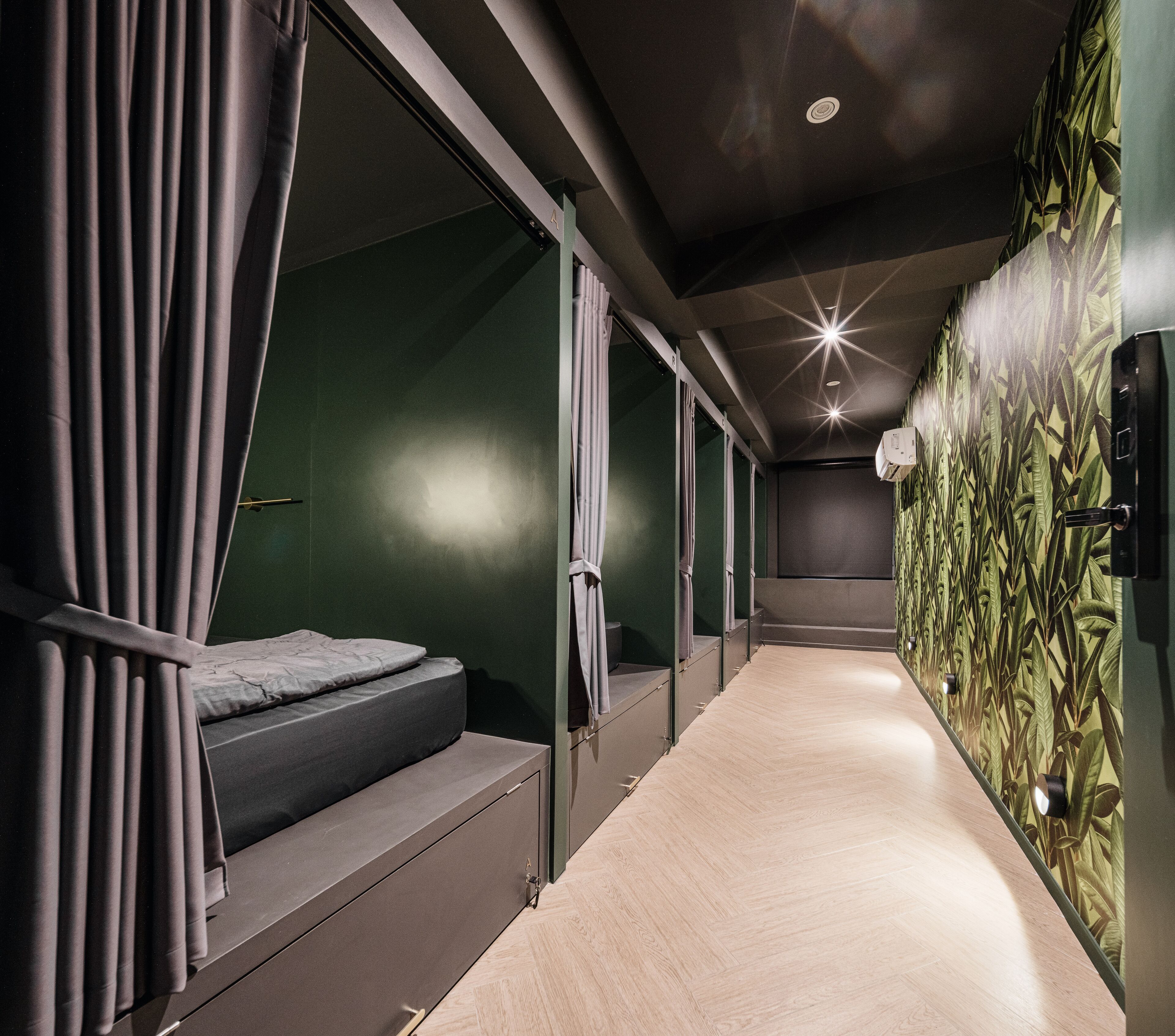 A narrow corridor with a bed on the left and a wall with a leaf pattern on the right.