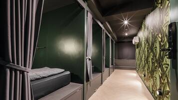 A narrow corridor with a bed on the left and a wall with a leaf pattern on the right.