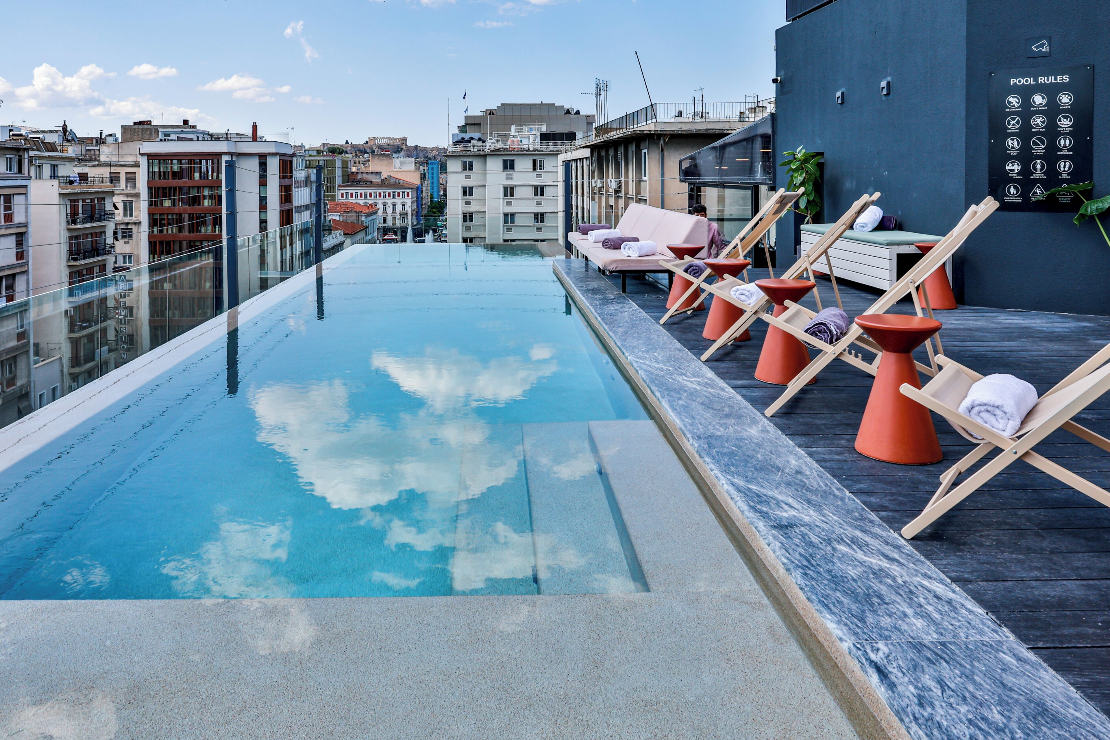 A rooftop pool with clear blue water, lounge chairs, and a view of the cityscape.
