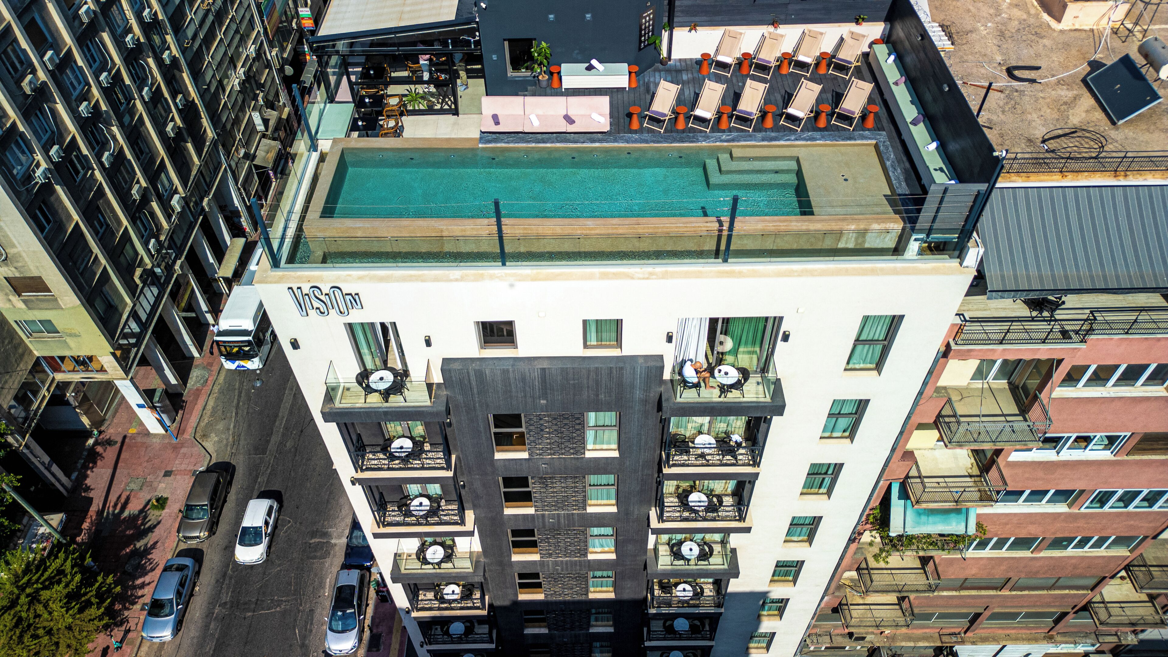 Un edificio alto con piscina en la azotea, varios balcones y un letrero visible que dice 'VISION'.
