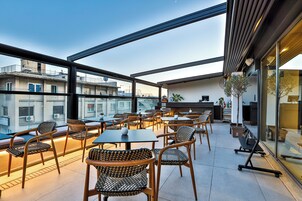 A rooftop terrace with outdoor seating, a bar area, and a view of the cityscape.