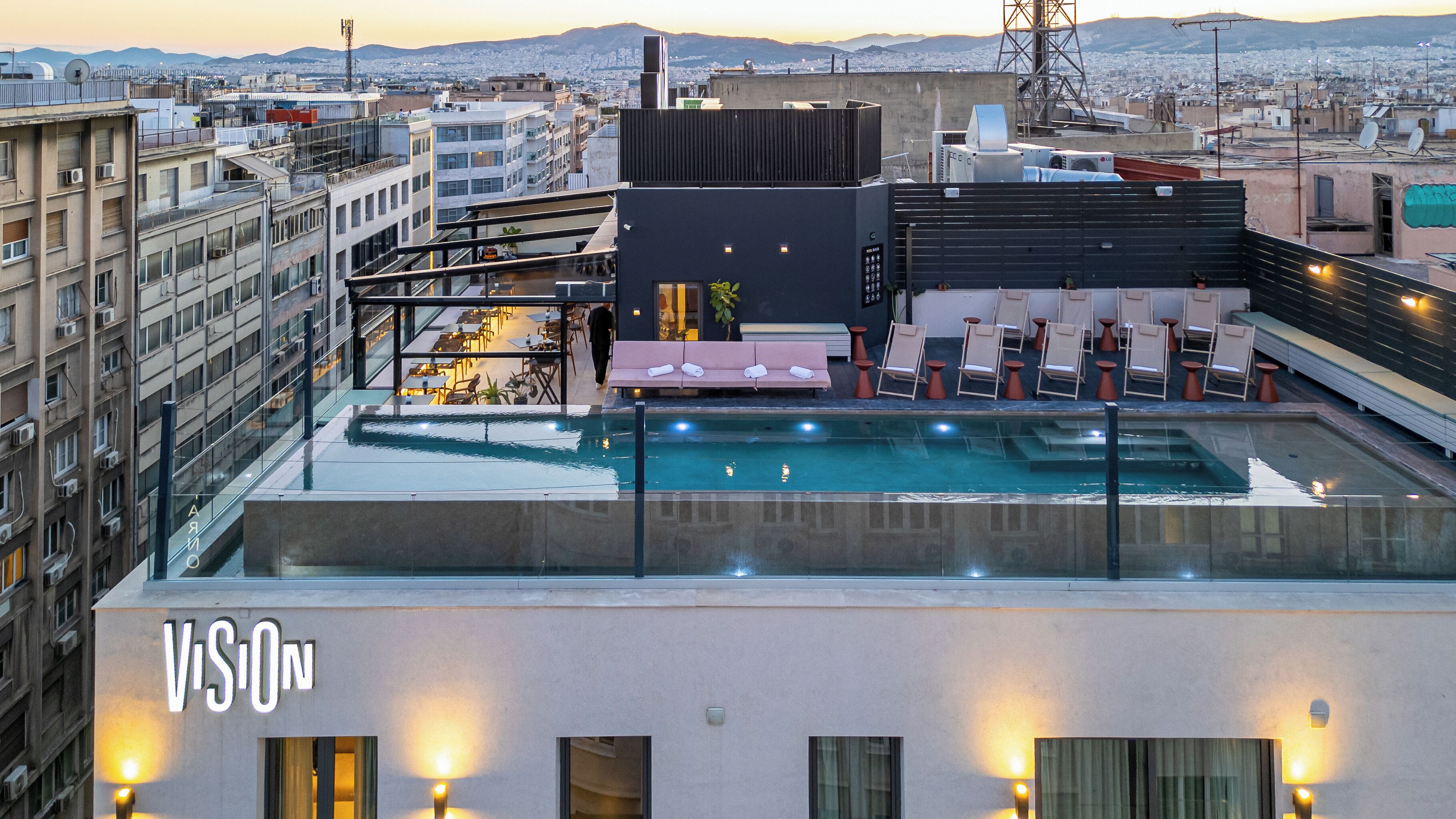 Une piscine sur le toit, dotée de chaises longues et d’un espace bar, le tout entouré d’immeubles urbains.