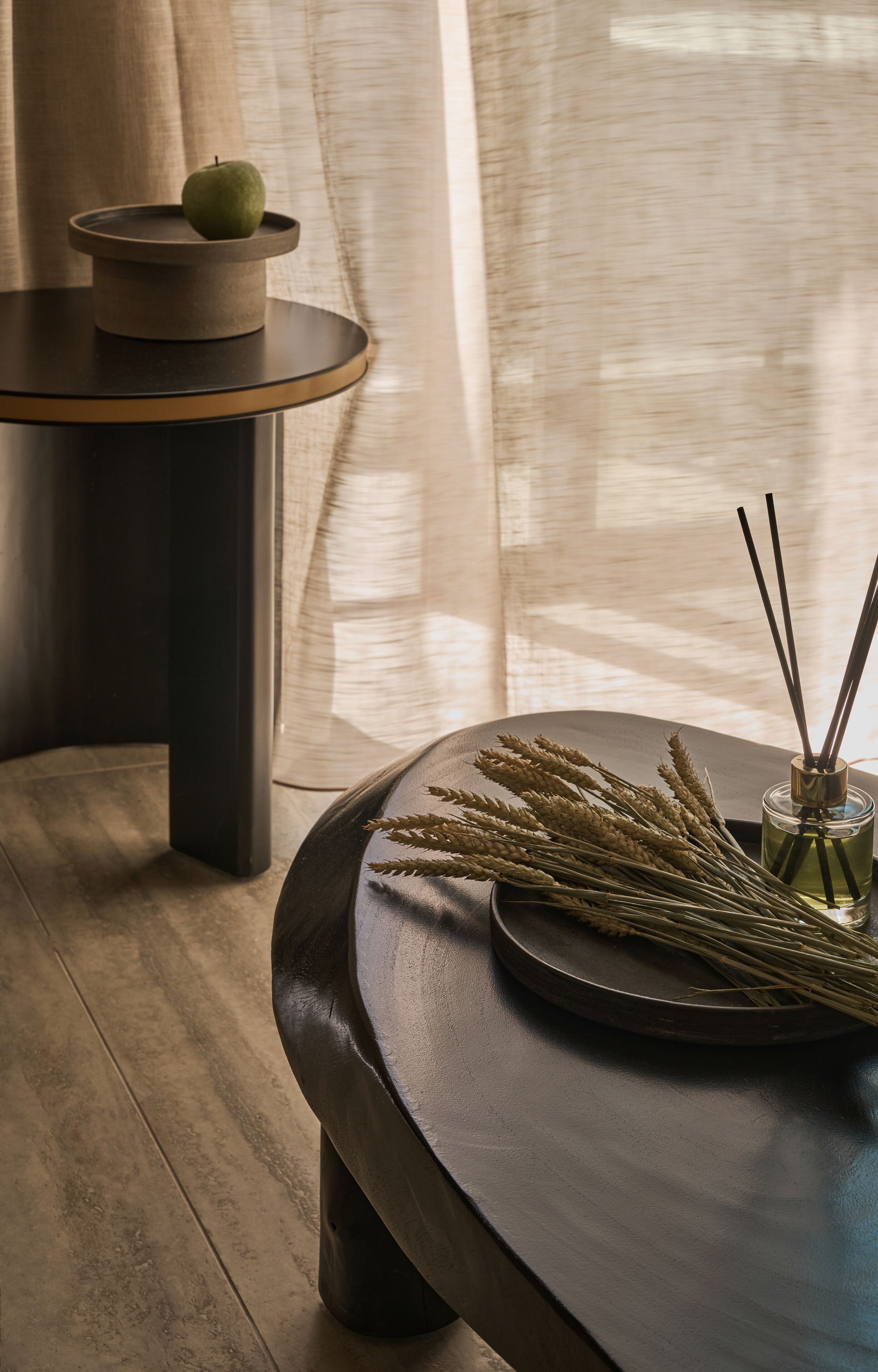 Una mesa redonda de madera con superficie oscura, una manzana verde sobre un atril de madera y un difusor de caña con recipiente de vidrio.