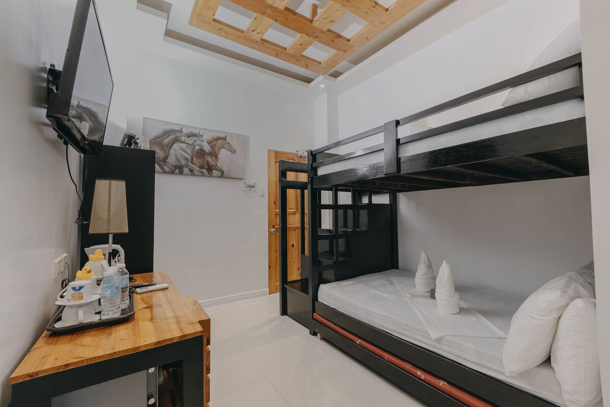 A bunk bed room with a wooden desk, a television, and a painting of horses.