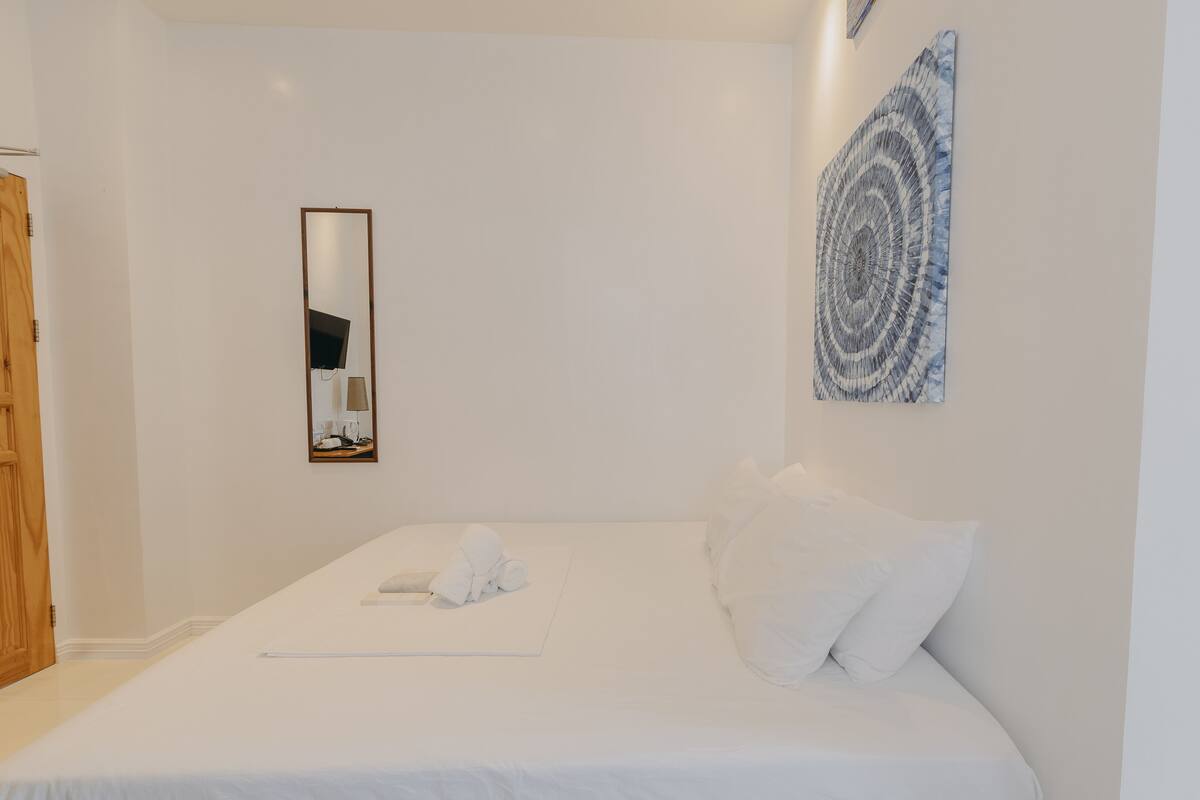 A neatly made bed with white linens and a towel, a wooden door, and a wall-mounted mirror.
