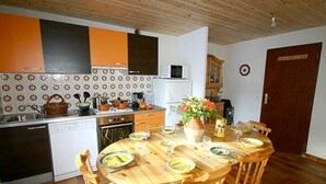 A kitchen with wooden cabinets, a microwave, a sink, and a dining table set for four. - Chalet LA Marmotte 5 (Risoul)