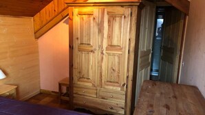 A wooden bedroom with a bed, a wooden wardrobe, and a small stool. - Chalet LA Marmotte 5 (Risoul)