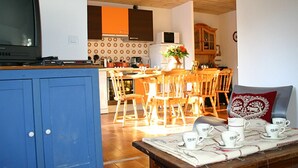 A kitchen with wooden cabinets, a dining area with a table set for four, and a television on a stand. - Chalet LA Marmotte 5 (Risoul)