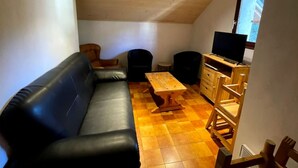 A cozy loft-style room with a black leather sofa, a wooden dining table, and a television on a wooden stand. - Chalet LA Marmotte 5 (Risoul)