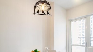 A dining area with a white table, chairs, a hanging light fixture, and a view of a building through a window.