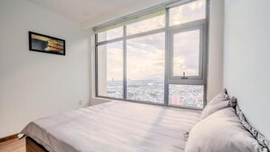 A bedroom with a large window, a bed, and a framed picture on the wall.